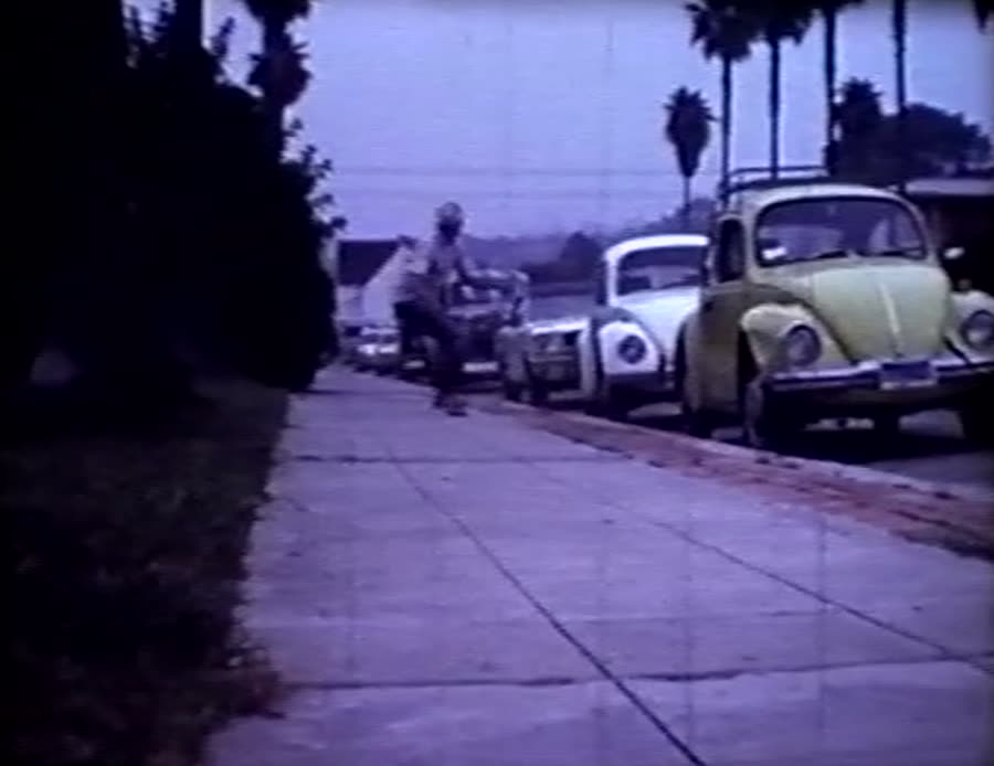 A yellow VW bug parked on a palm-lined street at dusk